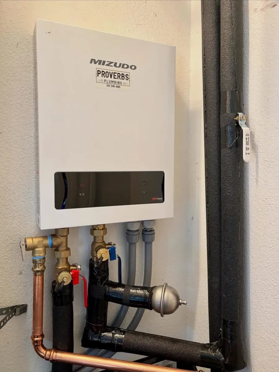 Wall-mounted Mizudo tankless water heater tagged by Proverbs Plumbing with new copper and braided supply lines below