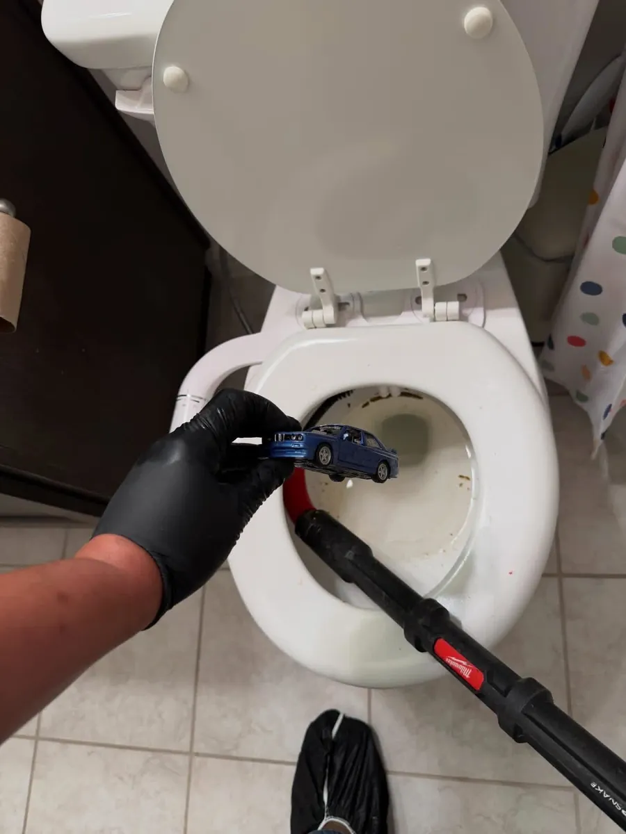 Gloved technician lifting a toy car out of a toilet bowl with a grabber tool